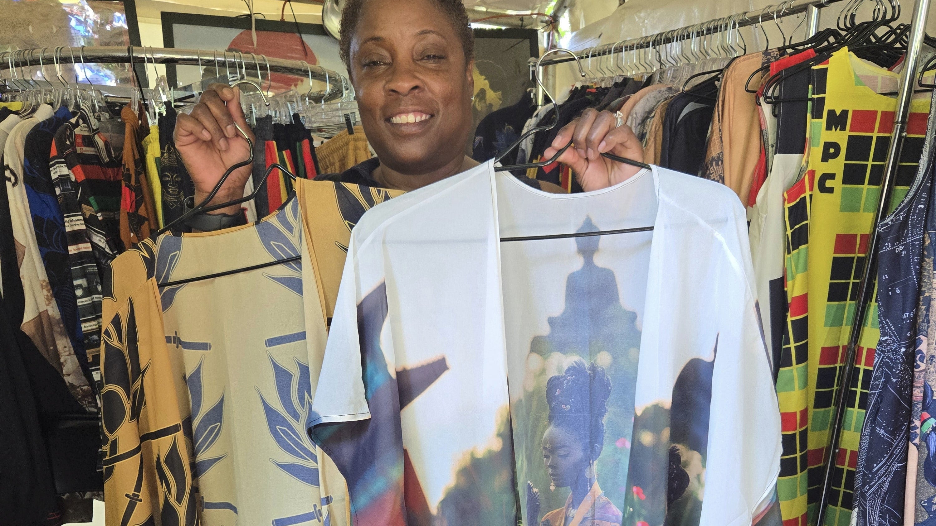 A happy customer purchasing  colorful items with patterns and designs, standing in front of a display of fabric.